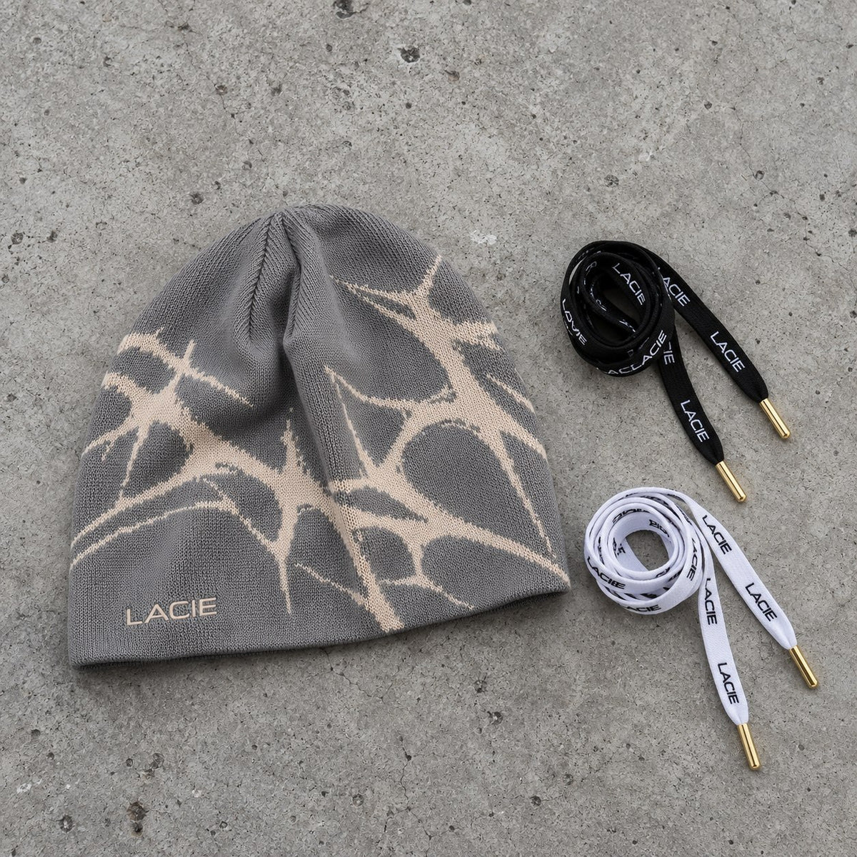 LACIE Thorn Beanie laid flat on concrete beside black and white LACIE laces
